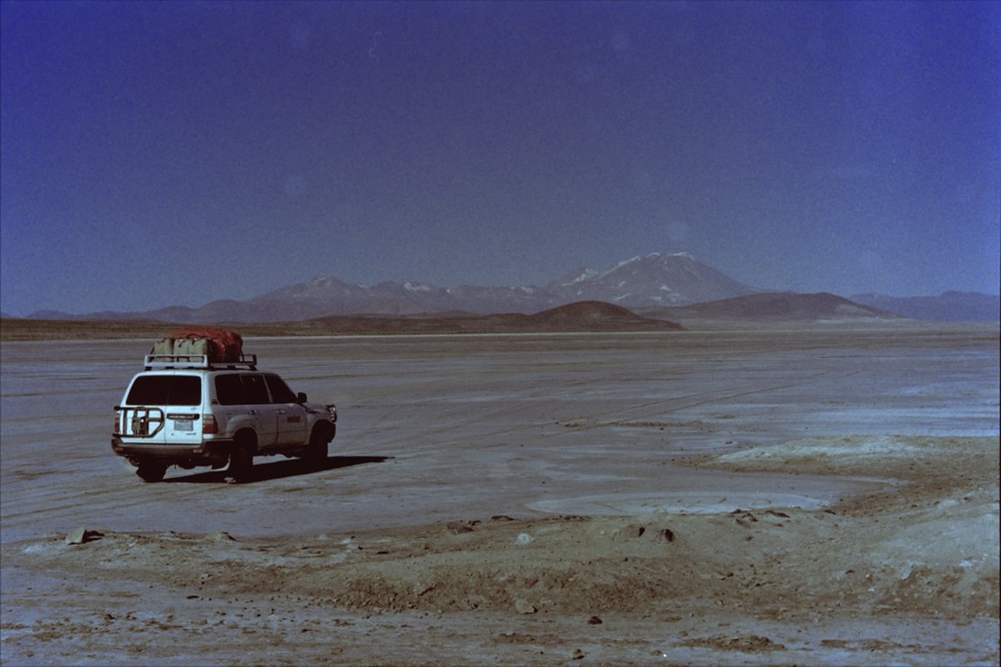 A loaded Land Cruiser parked on an empty plain below distant volcanoes