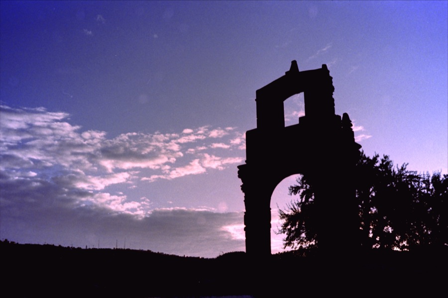 A ruined stone arch silhouetted against a violet dusk sky
