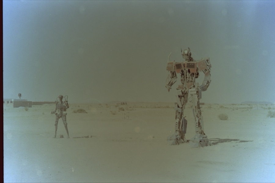 Two figures welded from scrap metal standing in an empty desert plain