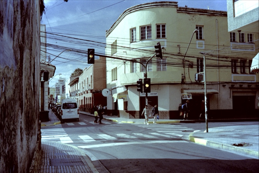 A street corner with traffic lights, tangled overhead cables and people crossing