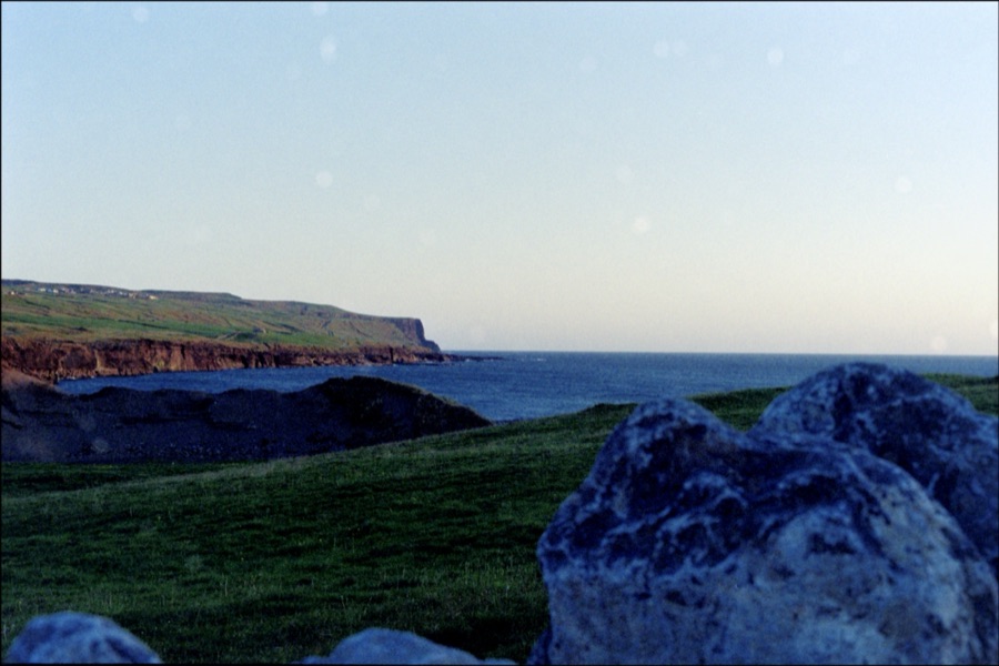 Large boulders in the foreground with distant cliffs and sea at dusk
