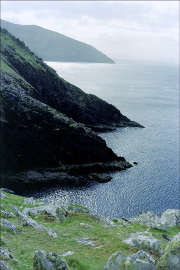 Steep sea cliffs dropping into a dark cove under a pale sky