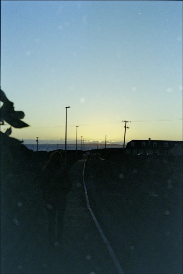 A figure silhouetted on a path leading towards the setting sun over the sea