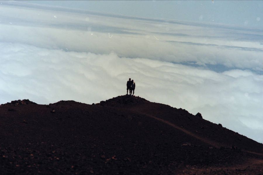 Two people silhouetted on a ridge above a sea of clouds